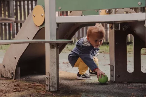 Un enfant ramasse une balle sous un toboggan