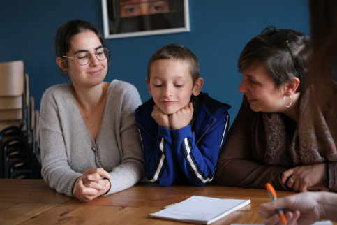 Deux adultes entourent un jeune face à un cahier