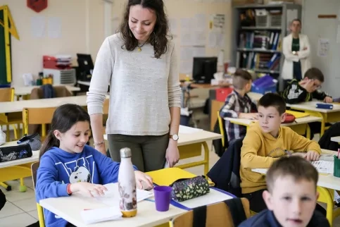 Dans une salle de classe, une maîtresse souris à une élève.